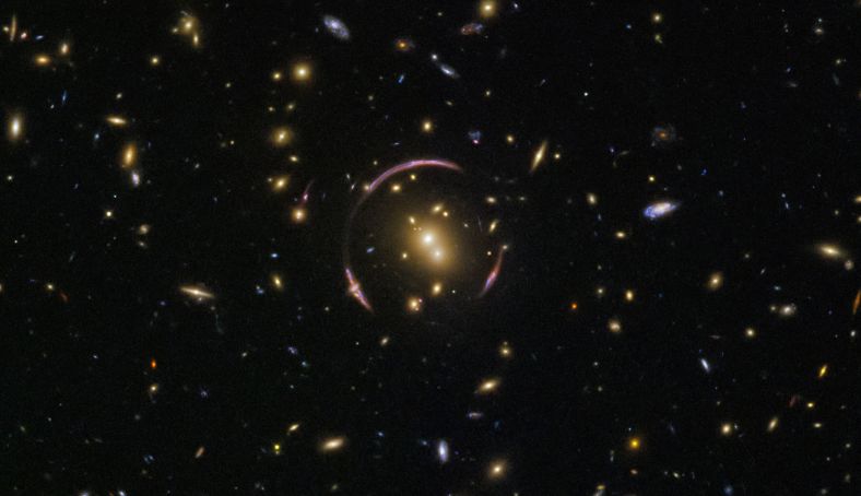 这个星系团编号SDSS J0146-0929，其中可以分辨出不少椭圆星系和螺旋星系。由于呈现给我们的角度各不相同，部分仅仅以星系平面的侧边缘朝向我们，部分星系平面则恰好是整个正对我们，将壮观的悬臂及其中的一切展露无遗。   实际上，SDSS J0146-0929包含数百个星系，它们在引力的作用下聚拢在一块。由于质量巨大，星系团周围的时空被严重扭曲，当来自遥远的天体——如星系——发出的光线，经过一个类似星系团等质量巨大的天体时，就出现类似的优雅的曲线，它们被称作“爱因斯坦环”。   在上面哈勃的照片中，背景星系发出的光线，在经过星系团SDSS J0146-0929后，被扭曲和改变方向，使得我们在地球上看起来，背景星系似乎同时出现在了多个不同的位置。
